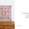 A red and white quilt featuring intricate, Japanese-inspired appliqué from "Kawaii Appliqué Quilts from Japan" by Schiffer Publishing, Ltd. is draped over a wooden chest. Nearby, text reads: “Part One: The Magical World of Kawaii.”.