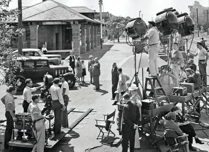 A black-and-white photo on the cover of "The Art of Classic Crime and Mystery Movies" by Schiffer Publishing, Ltd. shows a busy film crew with actors, vintage cars, and equipment outside the Santa Rosa train station.