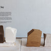 Five clay blocks in brown, white, tan, and gray are arranged on wood—ideal for beginners using Practical Pottery by Schiffer Publishing, Ltd. to select the best clay for ceramics projects.