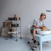 A woman creates pottery on a wheel, shaping clay into a pitcher, with finished ceramics displayed nearby. "Throw a Pitcher" is on the wall. Practical Pottery by Schiffer Publishing, Ltd. inspires the creative scene.