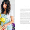 A woman with long dark hair, wearing a light blue floral dress over a white top, arranges yellow flowers on a wooden table beside "Starting Your Floral Design Studio" by Schiffer Publishing, Ltd., opened to its foreword page.