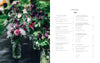 A row of glass jars with pink, purple, and white flowers sits on a dark outdoor table; next to them is "Starting Your Floral Design Studio" by Schiffer Publishing, Ltd., opened to the contents page on floral techniques and eco-friendly arranging.