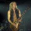 A long-haired guitarist rocks on stage in a black vest, with drums and Marshall amps behind him—echoing the legendary Dio “Holy Diver” era, now captured in DIO: The Unholy Scriptures from Schiffer Publishing, Ltd.