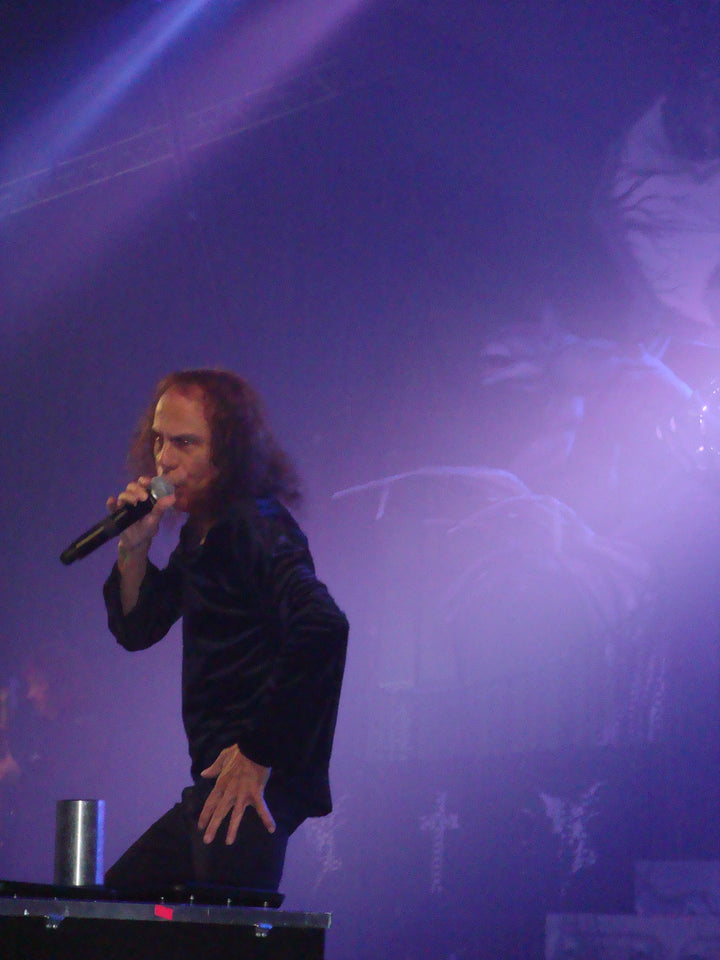 A male rock singer with long hair passionately performs on stage, echoing Ronnie James Dio as he belts out "Holy Diver," purple lights and fog evoking the Dio band vibe—just like the spirit captured in Schiffer Publishing, Ltd.'s DIO: The Unholy Scriptures.