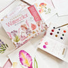 The Watercolor the Easy Way Paint-Your-Own Watercolor Cards Flowers kit by Schiffer Publishing, Ltd. is displayed with paints, a brush, flower illustrations, finished floral artworks, and charming watercolor notecards on a white surface.
