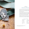 A silver abstract brooch with engraved leaves and a face sits on green fabric beside "Projects and Techniques for Metal Clay Jewelry" from Schiffer Publishing, Ltd., showcasing detailed jewelry craftsmanship.