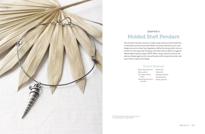 The book "Projects and Techniques for Metal Clay Jewelry" by Schiffer Publishing, Ltd. is shown on a beige palm leaf alongside instructions and materials, its cover featuring an elegant metal choker with a spiral shell pendant.