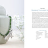 A silver pendant necklace with green beads rests on a pale green ceramic container. In the softly blurred background is Projects and Techniques for Metal Clay Jewelry by Schiffer Publishing, Ltd., open to a page about silver jewelry.