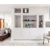 A stylish living area with a built-in white shelving unit displays colorful décor—perfect inspiration from PowerHouse by Schiffer Publishing, Ltd. A beige armchair is up front; a sofa with pillows sits by the large windows on the left.