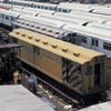 In "New York Subways and Stations, 1970–1990" by Schiffer Publishing, Ltd., a yellow and brown maintenance train car rests amid debris in a rail yard, flanked by white subway cars covered in graffiti.