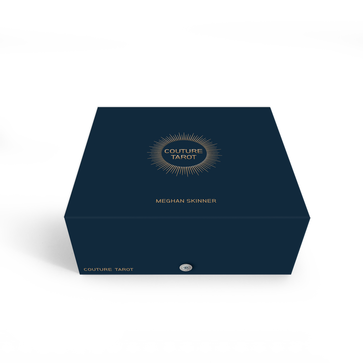 A dark blue Couture Tarot box by Schiffer Publishing, Ltd., features gold text and a sunburst design on the lid, with "Couture Tarot" in gold on the side set against a minimalist white background.