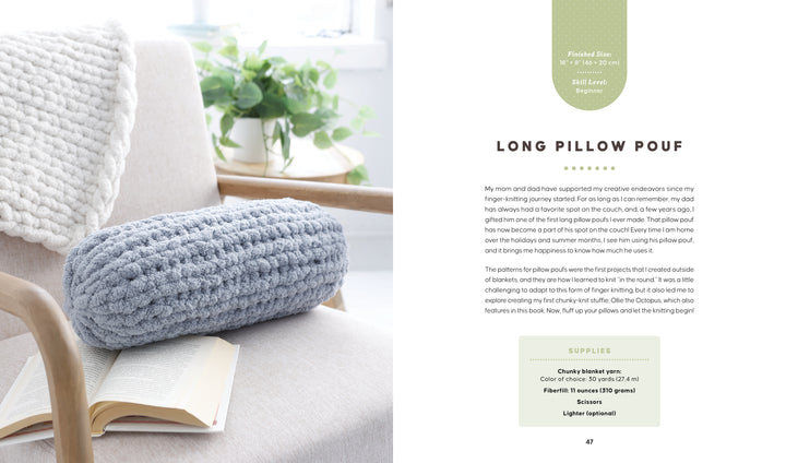 A beige armchair holds an open book and a chunky knit gray pillow pouf, inspired by "Get Started in Finger Knitting" from Schiffer Publishing, Ltd., basking in soft natural light with a cream blanket draped over the chair’s back.