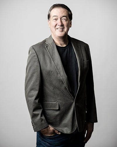 A man with short dark hair in a gray blazer, black shirt, and blue jeans smiles with one hand in his pocket against a plain background, echoing the style found in "Robert C. Jackson" by Schiffer Publishing, Ltd.