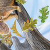 A curious squirrel clings to a tree branch amid autumn leaves and acorns, celebrating the acorn’s life cycle. Against a soft blue sky, the text reads: “Greatness begins in the tiniest places.” The Tiniest Giant by Schiffer Publishing, Ltd.