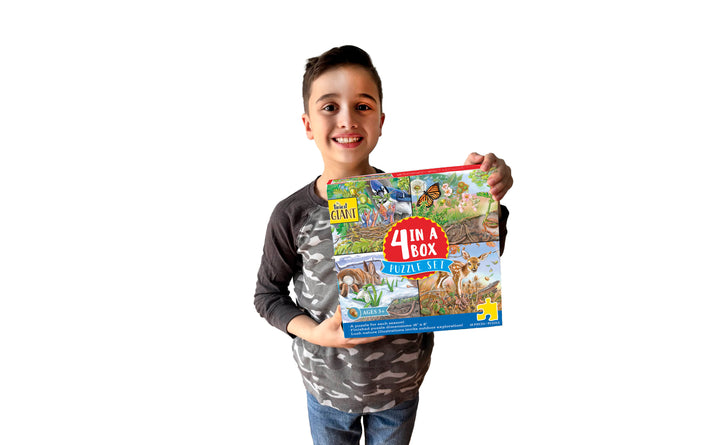 A smiling child with dark hair and a gray and black shirt holds The Tiniest Giant 4-in-1 Puzzle Set by Schiffer Publishing, Ltd., featuring colorful dinosaurs and jungle scenes. White background.