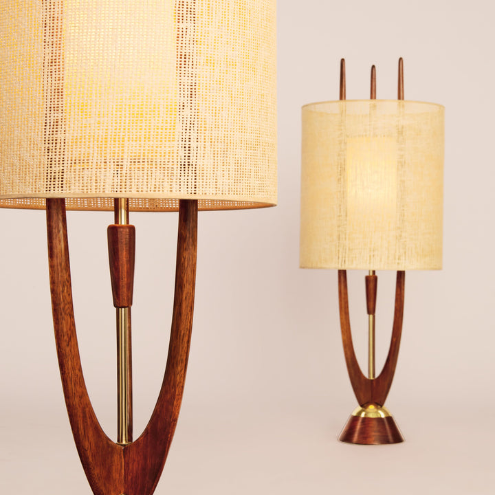 Two mid-century modern table lamps with wooden bases, gold accents, and cylindrical fabric shades, inspired by the Modeline of California from Schiffer Publishing, Ltd. One lamp is in focus; the other is blurred against a light background.