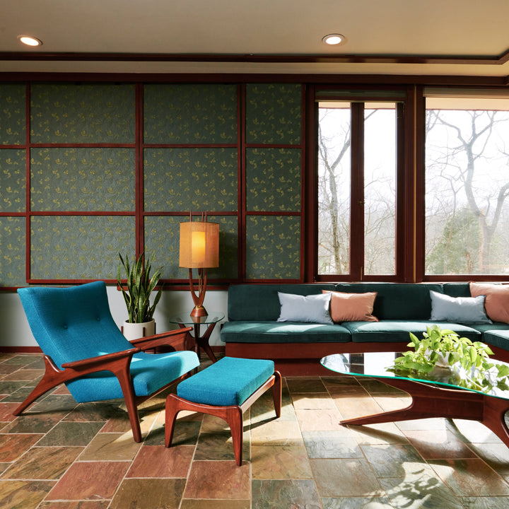 A mid-century modern living room features a teal lounge chair, ottoman, and built-in sofa. The Modeline of California by Schiffer Publishing, Ltd. adds cozy lighting, while warm accents and greenery complete this stylish space.