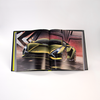 An open copy of Automobili Lamborghini by Schiffer Publishing, Ltd. reveals a full-page photo of a sleek, metallic green sports car with angular lines and dramatic lighting, set against geometric metal structures for a striking modern effect.