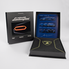 The Automobili Lamborghini Special Edition by Schiffer Publishing, Ltd. is presented in an open black and gold box with Lamborghini branding, revealing a book filled with blue luxury sportscar images and a signature.