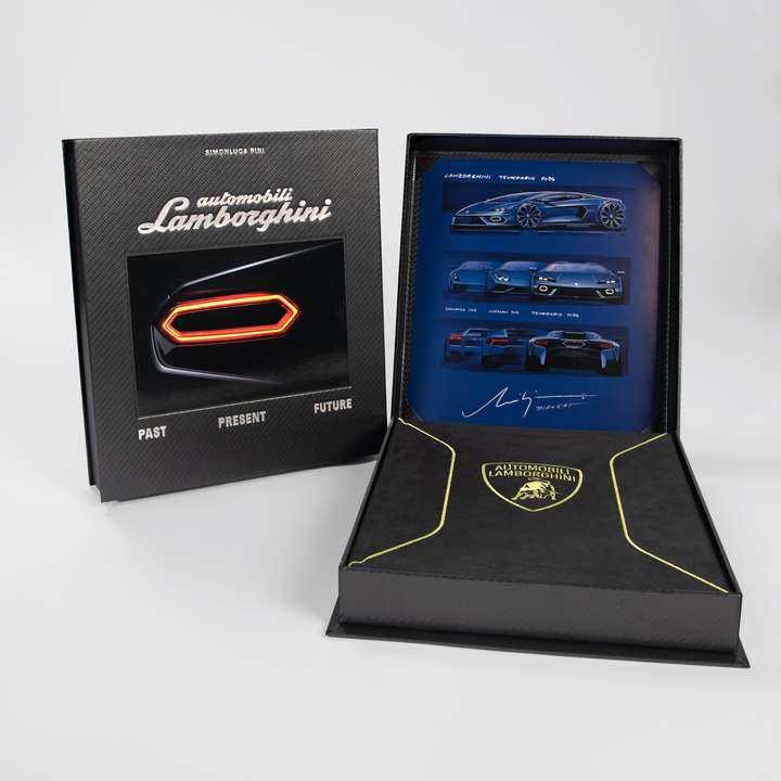 The Automobili Lamborghini Special Edition by Schiffer Publishing, Ltd. is presented in an open black and gold box with Lamborghini branding, revealing a book filled with blue luxury sportscar images and a signature.