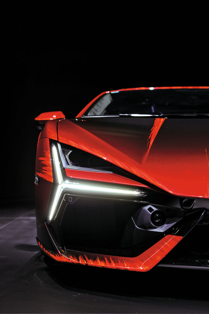 Close-up of the front left side of a red Automobili Lamborghini Special Edition sportscar with angular LED headlights and sharp lines, set against a dark background—a tribute from Schiffer Publishing, Ltd.