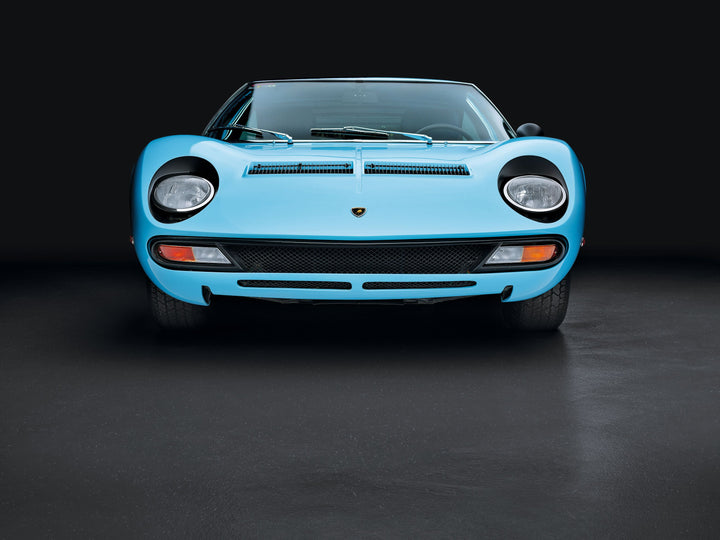 A front view of the blue Automobili Lamborghini Special Edition from Schiffer Publishing, Ltd., shown against a black background with its headlights, grille, and windshield visible—a true icon among luxury sports cars.