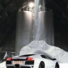 An Automobili Lamborghini Special Edition by Schiffer Publishing, Ltd. is parked inside a spacious industrial building with white powder beneath silos and a stream of material falling from above.