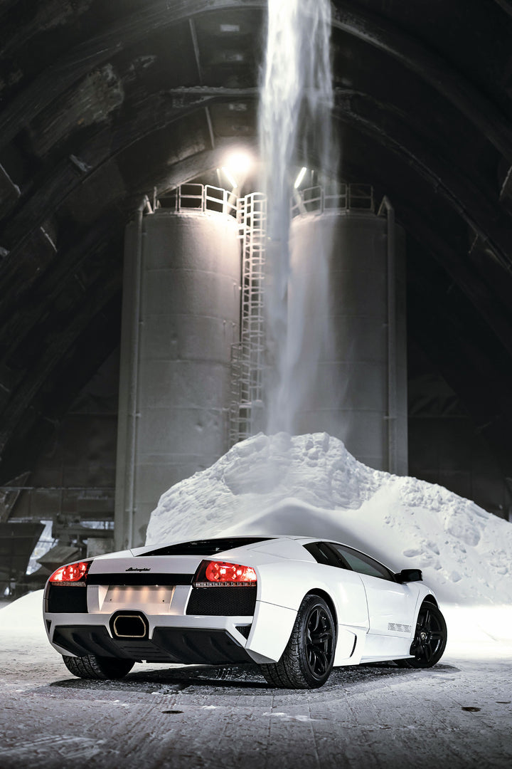 An Automobili Lamborghini Special Edition by Schiffer Publishing, Ltd. is parked inside a spacious industrial building with white powder beneath silos and a stream of material falling from above.