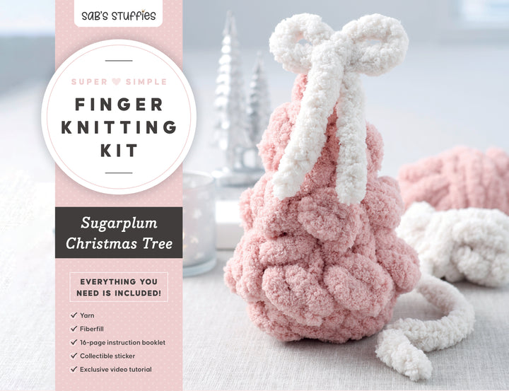 A pink, textured, handcrafted Christmas tree with a white yarn bow sits on a table beside the Super Simple Finger Knitting Kit Sugarplum Christmas Tree by Schiffer Publishing, Ltd., showing its included items.