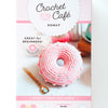 The Crochet Cafe Amigurumi Kit Donut by Schiffer Publishing, Ltd. features a pink and white crochet donut and includes yarn, stitch marker, crochet hook, needle, and fiberfill—ideal for beginner crochet enthusiasts.