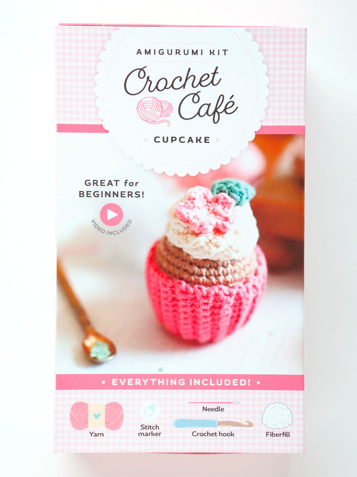 The Schiffer Publishing, Ltd. Crochet Cafe Amigurumi Kit Cupcake is a pink and white box with a cupcake image. It includes yarn, stitch marker, crochet hook, needle, and fiberfill—great for beginners.