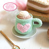 The Crochet Cafe Amigurumi Kit Hot Cocoa by Schiffer Publishing, Ltd. includes all you need to crochet a mug with a pink heart, marshmallow top, gold spoon, and yarn cake—perfect for crafting 1 cute hot cocoa amigurumi!.