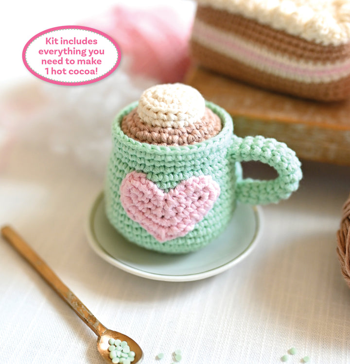 The Crochet Cafe Amigurumi Kit Hot Cocoa by Schiffer Publishing, Ltd. includes all you need to crochet a mug with a pink heart, marshmallow top, gold spoon, and yarn cake—perfect for crafting 1 cute hot cocoa amigurumi!.