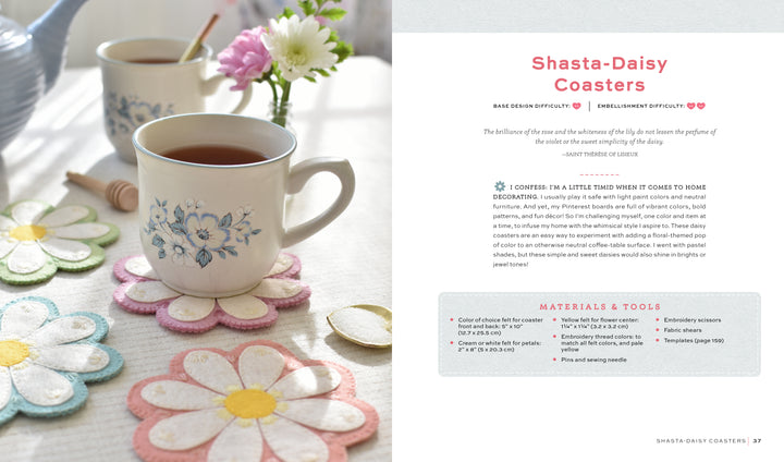 A cup of tea in a white mug with blue flowers sits on a colorful daisy-shaped felt coaster—a fun beginner project from "HeartFELT Crafts to Make and Give" by Schiffer Publishing, Ltd. More coasters, a saucer, and another mug are on the sunlit table.