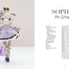 A crocheted giraffe doll in a purple dress stands on a white surface, with purple flowers to the left and Schiffer Publishing’s "Sweet and Simple Amigurumi Friends" amigurumi pattern for Sophia the Giraffe to the right.