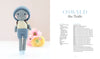 A blue-shelled crocheted turtle with a gray body, yellow-striped shirt, and blue pants stands beside pastel flowers. The crochet book "Sweet and Simple Amigurumi Friends" by Schiffer Publishing, Ltd. shows amigurumi instructions.