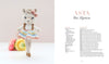 A crocheted alpaca doll in a pastel tutu and bow stands on one leg by a yellow flower; on the right is the book "Sweet and Simple Amigurumi Friends" from Schiffer Publishing, Ltd., featuring amigurumi patterns and instructions.