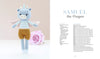 A crocheted blue dragon with wings and brown shorts stands next to a pink rose. The pattern for Samuel the Dragon is featured in "Sweet and Simple Amigurumi Friends" by Schiffer Publishing, Ltd., with full materials and instructions included.