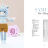 A crocheted blue dragon with wings and brown shorts stands next to a pink rose. The pattern for Samuel the Dragon is featured in "Sweet and Simple Amigurumi Friends" by Schiffer Publishing, Ltd., with full materials and instructions included.