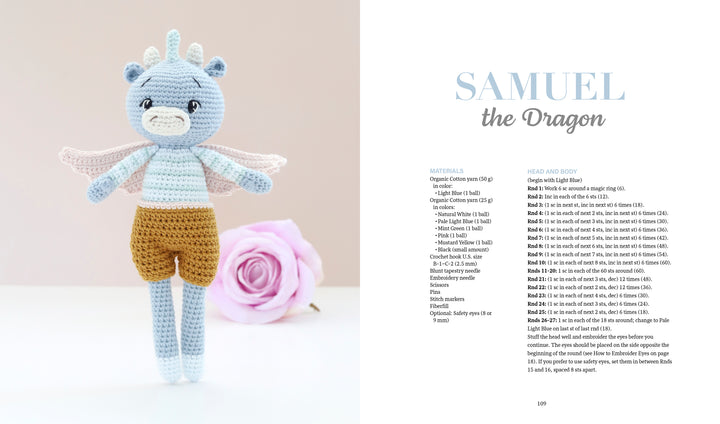A crocheted blue dragon with wings and brown shorts stands next to a pink rose. The pattern for Samuel the Dragon is featured in "Sweet and Simple Amigurumi Friends" by Schiffer Publishing, Ltd., with full materials and instructions included.