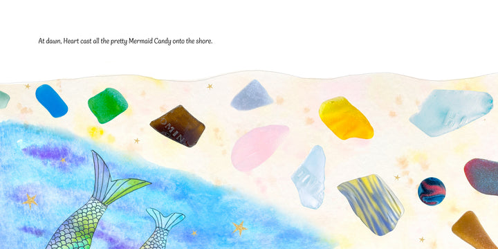 Mermaid tails rise from blue waves near a sandy shore sparkling with sea glass and golden stars. Text: At dawn, Heart scattered Mermaid Candy by Schiffer Publishing, Ltd. along the shore in this magical mermaid picture book.