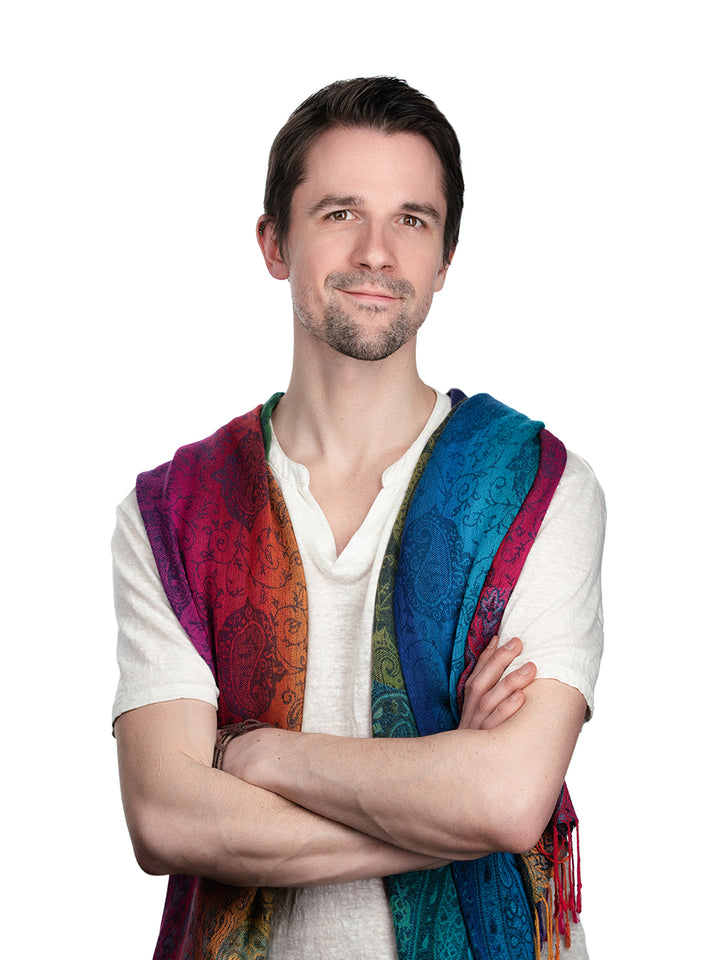 A man with short brown hair and light stubble stands with arms crossed, smiling slightly, wearing a white shirt and a colorful Patch Tarot-inspired scarf. He is against a plain white background. Patch Tarot by Schiffer Publishing, Ltd.