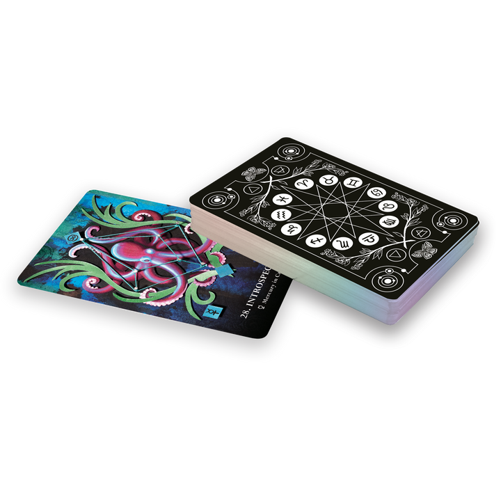 A stack of The MicroCosmic Oracle cards by Schiffer Publishing, Ltd. features intricate black and white geometric backs. One card is face up, revealing a vibrant abstract design with swirling shapes on a blue and green background.
