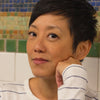 A person with short dark hair wearing a white shirt with blue stripes sits before a mosaic wall inspired by New York MTA Arts & Design, evoking the style featured in "Museum in Transit" by Schiffer Publishing, Ltd.