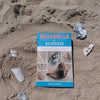 Seashells of Delmarva by Schiffer Publishing, Ltd. rests on the sand among shells, its cover showcasing Maryland and Virginia specimens—a perfect beachcombing guide.