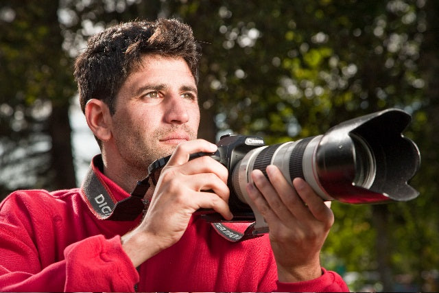 A man in a red jacket holds a camera outdoors, evoking the adventurous vibe of Pacific Northwest beverage culture showcased in "Drinkin' Up the Pacific Northwest" by Schiffer Publishing, Ltd.