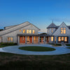Shingle Style Houses by Schiffer Publishing, Ltd. features large modern gray homes with multiple peaked roofs, warmly lit windows, circular driveways, and manicured lawns highlighted at dusk.