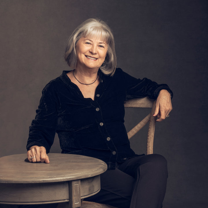 A woman sits at a table smiling as she plans her next adventure with "Oregon Waterfalls" by Schiffer Publishing, Ltd., eager to capture stunning waterfall photography at scenic Oregon locations.