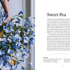 A woman in a blue-and-white striped dress holds a large bouquet of blue and white paper flowers beside a page from "Paper Flower Magic" by Schiffer Publishing, Ltd., displaying instructions for making crepe-paper blooms.