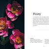 Three bright pink peony paper flowers with yellow centers rest on a dark surface beside a white sheet displaying "Paper Flower Magic" by Schiffer Publishing, Ltd., descriptive text, and a list of materials for paper flower crafting.